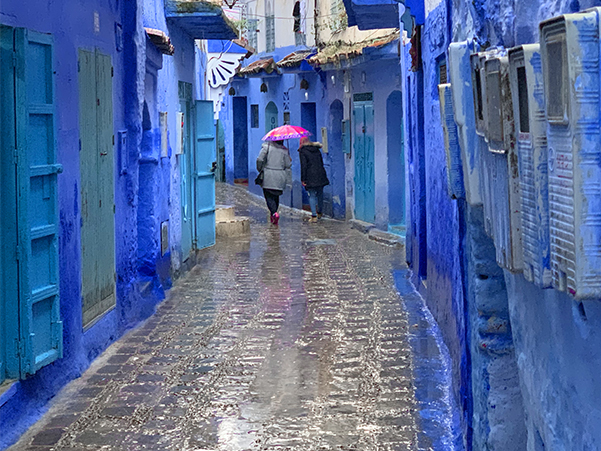 Foto Friday - a woman with a bright umbrella waling past blue-painted buildings