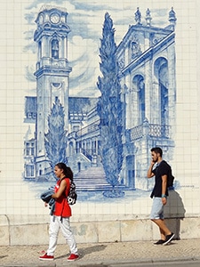 two people walking past colorful tiles on a wall