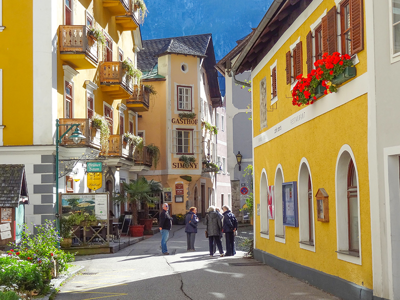people on a street with ellow builings seen in Hallstatt
