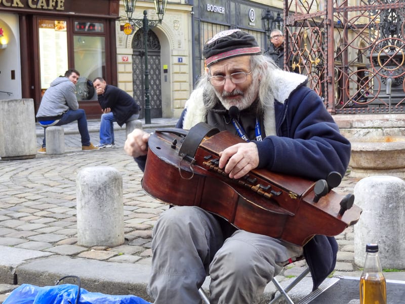 a bearded man playing a musical instrument on a sidewalk