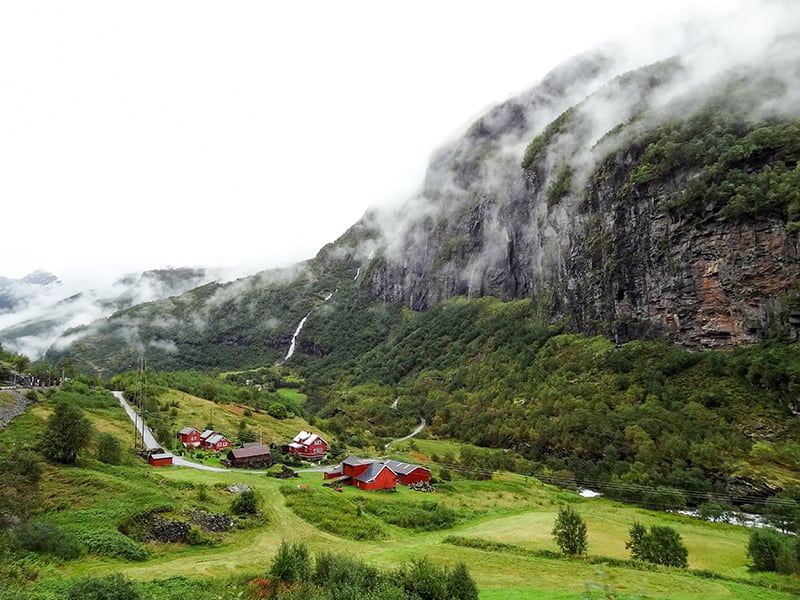 house in a valley below a large mountain seen when traveling on the Flam Railway