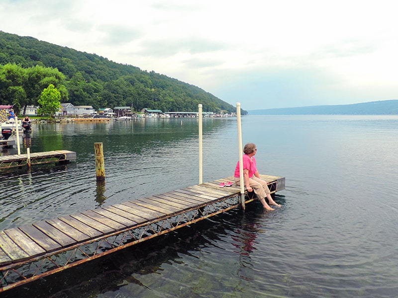 a woman sitting on a dock looking at the lake - one of the things to do in the Finger Lakes