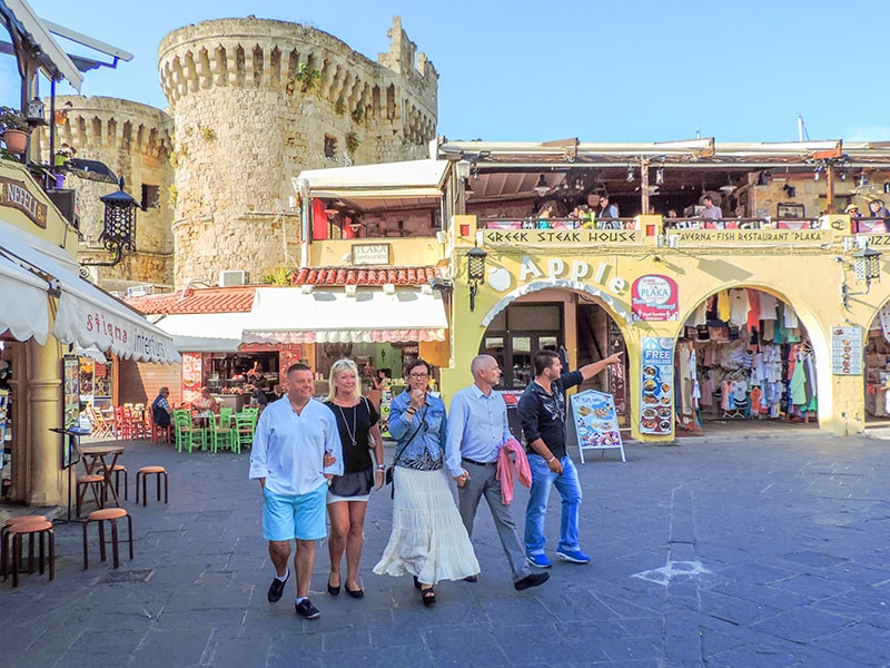people walking by an old castle in Rhodes, Greece