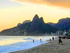people going in to the ocean at sunset with mountains behind them