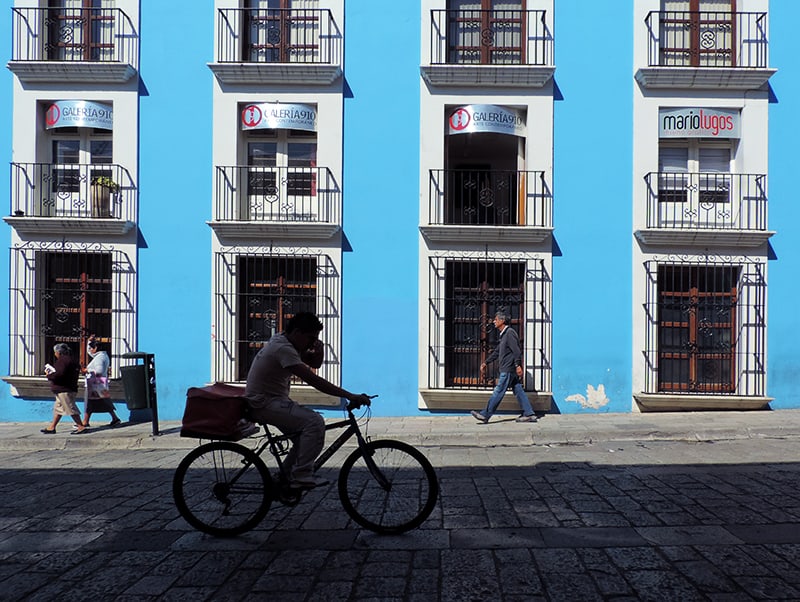 a boy riding a bike in front of a blue building, one of the things to do in oaxaca