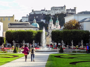 people walking in a park towards a fountain with an old vity in the distance