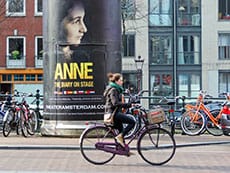 a young woman on a bicycle passing an advertising poster