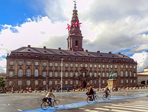 bicyclists riding past an old building with a spire