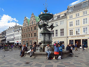 people sitting around a fountain by old buildings
