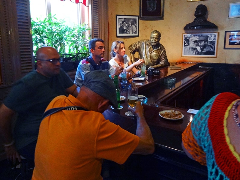 people at a bar with a statue of Hemingway