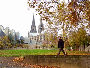 man walking in a park with the spires of a cathedral nearby