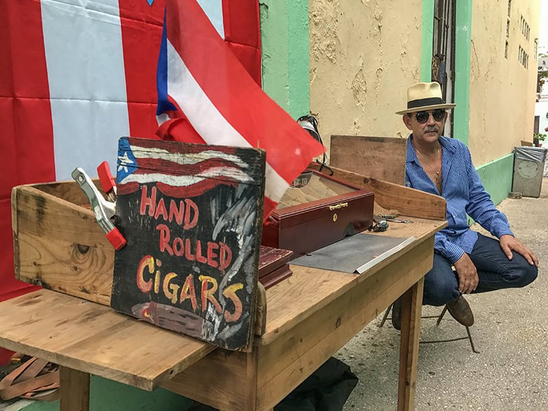 a man with a hat sitting while selling hand-rolled cigars