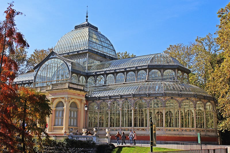 people walking past an ornate glass building in Retiro Park, one of the things to do in Madrid