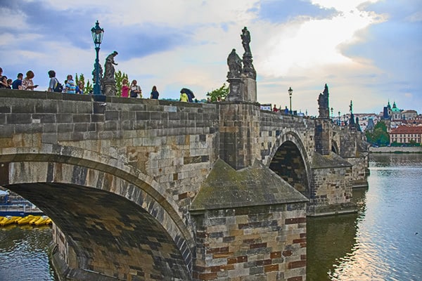people on a long stone bridge in the evening - berlin to prague train