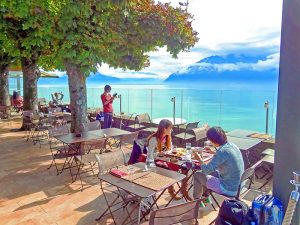 people on the terrace café of Le Baron Tevernier Hôtel looking out upon the Swiss Riviera