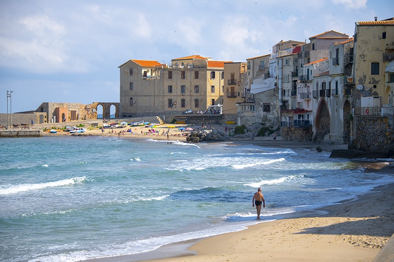 a man walking along the beach in Cefalu, one of the hidden gems in Italy