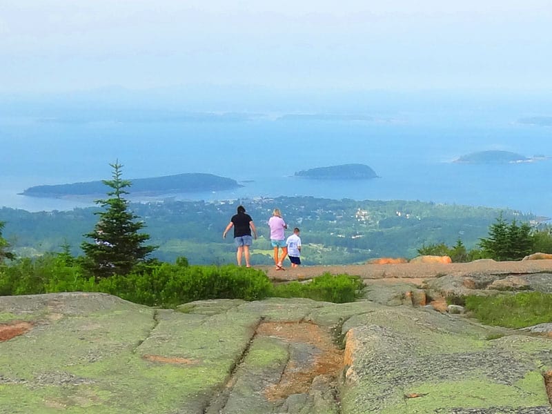 people on a mountain top looking out over the ocean in Acadia National Park, reached near the northern end of Maine Route 1