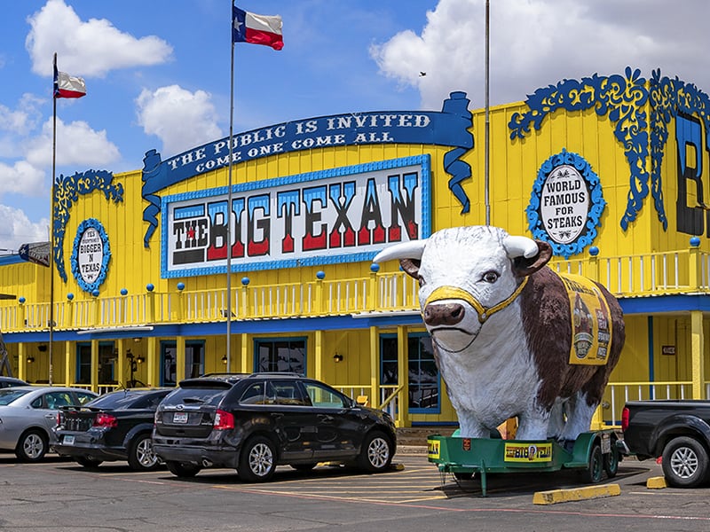 The outisde of a restaurant with a large cow sculpture