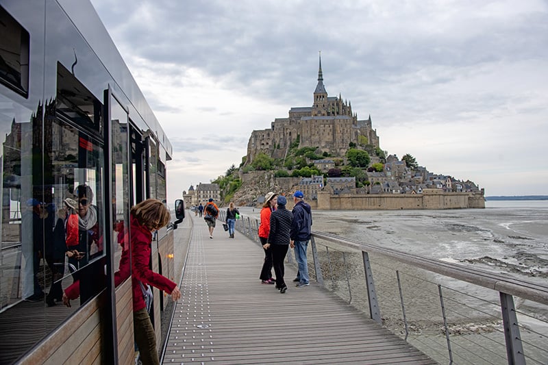 people on a causeway walking towards their Mont Saint-Michel hotel
