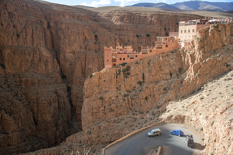 cars passing a hotel on a rock outcrop, a place to visit in Morocco