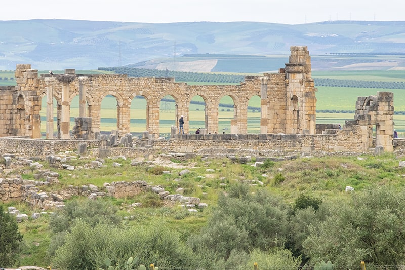 people exploring the ruins of an old Roam city, an interesting place to visit in Morocco 