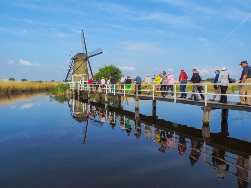 people walking across a bridge towards a windmill