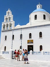 people walking past a white church on Santorini