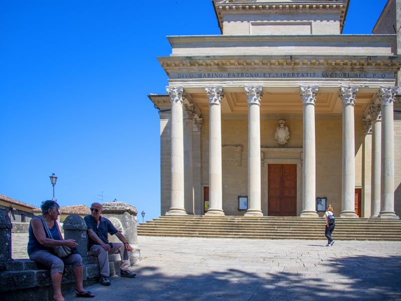 people sitting outside a basilica with large columns