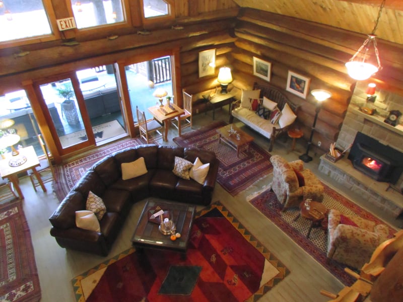 a great room made of logs with chairs and sofas by a fireplace in the Trout Point Lodge