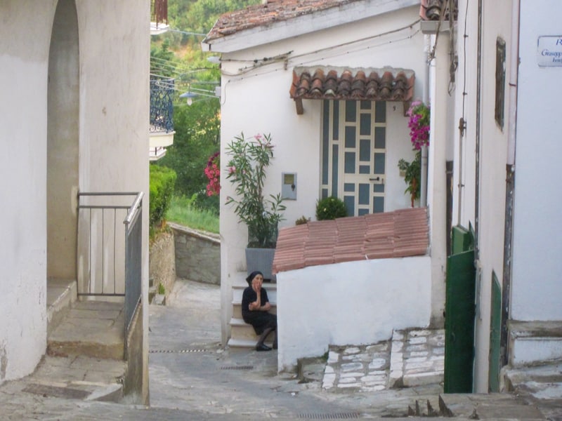 A woman sitting on steps on a small street in Accettura