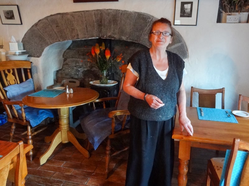 A woman standing by a table by a fireplace