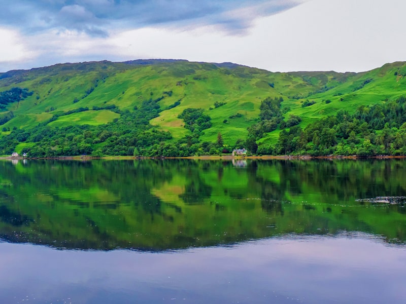 A large lake and green hills seen on a Highlands of Scotland road trip