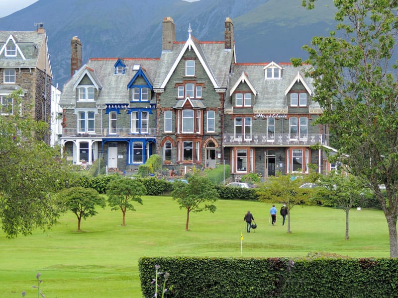 people walking across a park by beautiful old houses