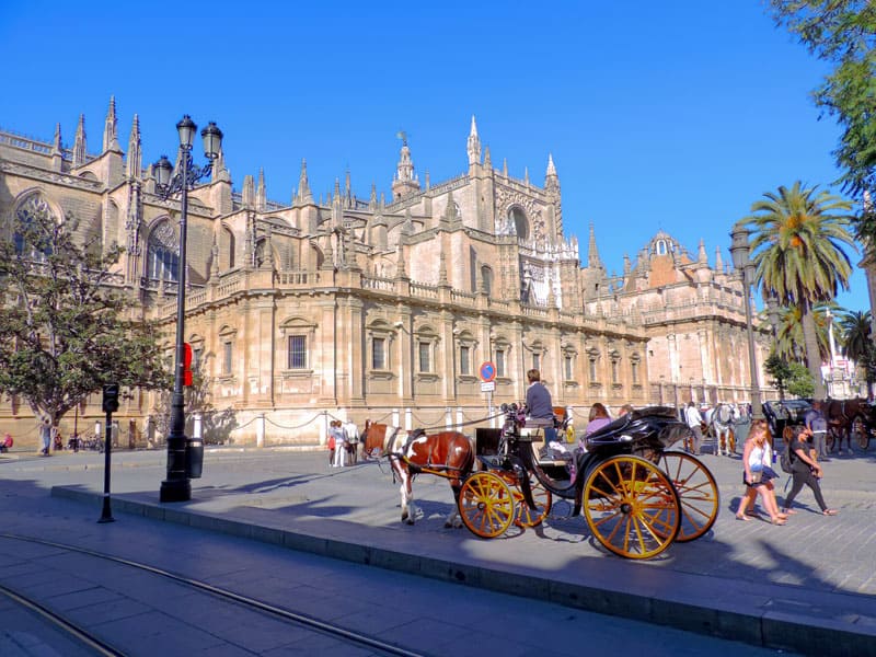 people in a horse-drawn carriage near an ornate building,  one of the things to do in Seville