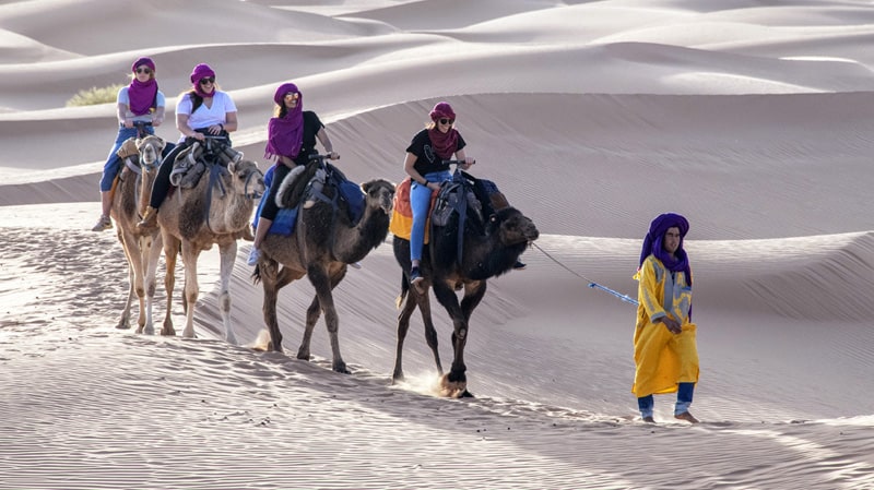 people camel trekking in Morocco being led by a man in a yellow robe