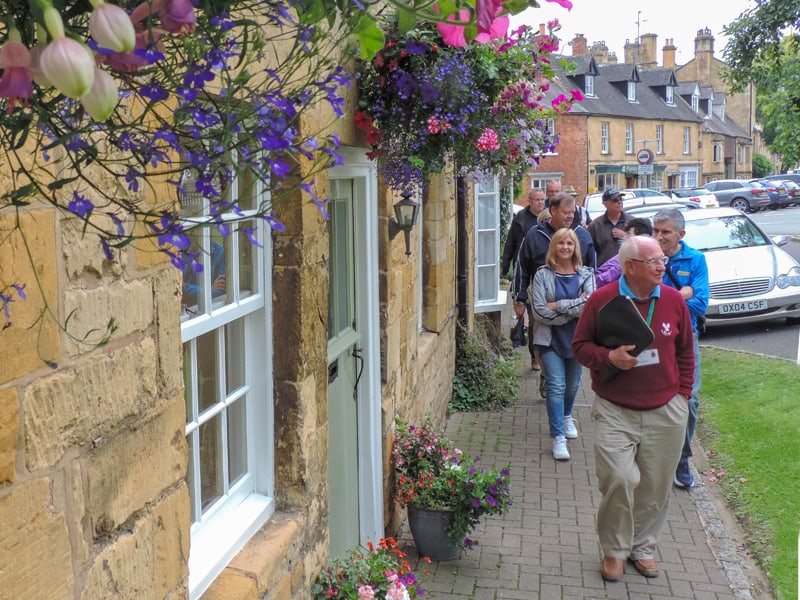 people walking by colorful flowers on a building