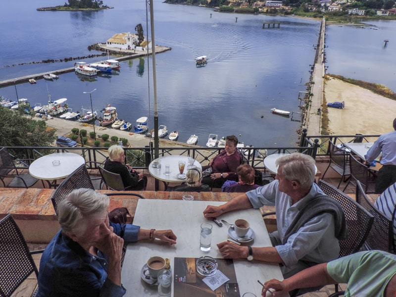 people having coffee on a balcony overlooking an island – one of the things to do in Corfu