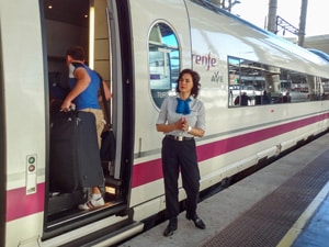 a female conductor helping people aboard on a European train trip