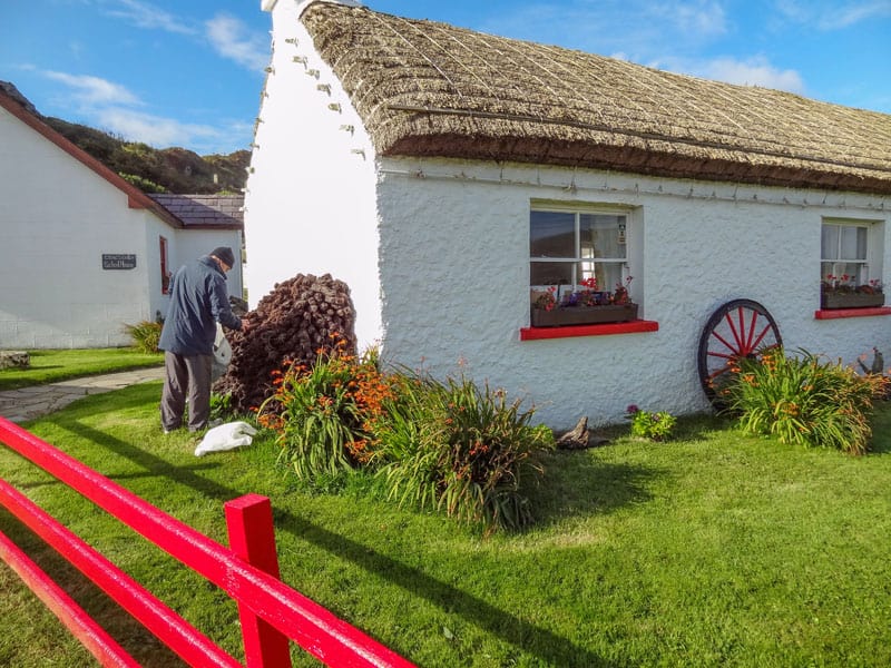 a red fence outisde a thatched roof white cottage