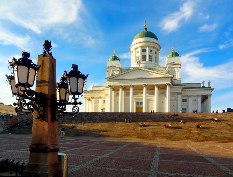 people sitting on the steps of an old cathedral on Senate Square, one of the things to do in Helsinki