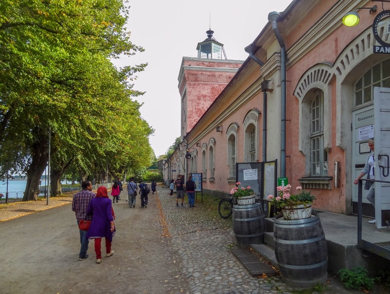 people waling past old buildings in a fortress