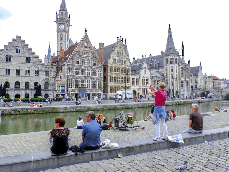 people sitting alongside a canal admiring ancient buildings, one of the things to do in Ghent