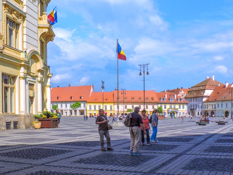 people walking about a large colorful town square, one of the things to do in Romania