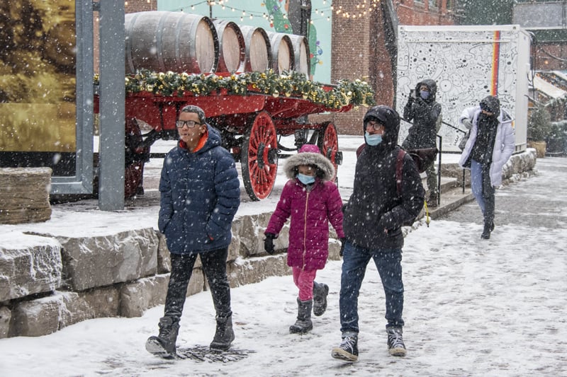 people walking in falling snow past a large red cart with wooden barrels seen in Toronto in the winter