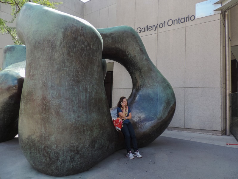 a woman on a phone sitting on a sculpture outside a museum