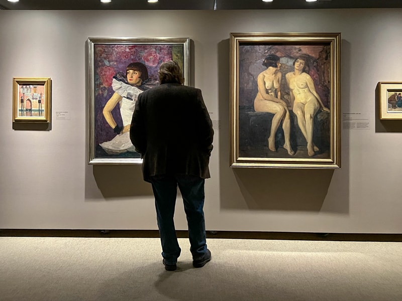 a man looking at paintings on a wall in a museum