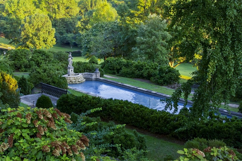 a statue by a pool in a large area of lawn and woods