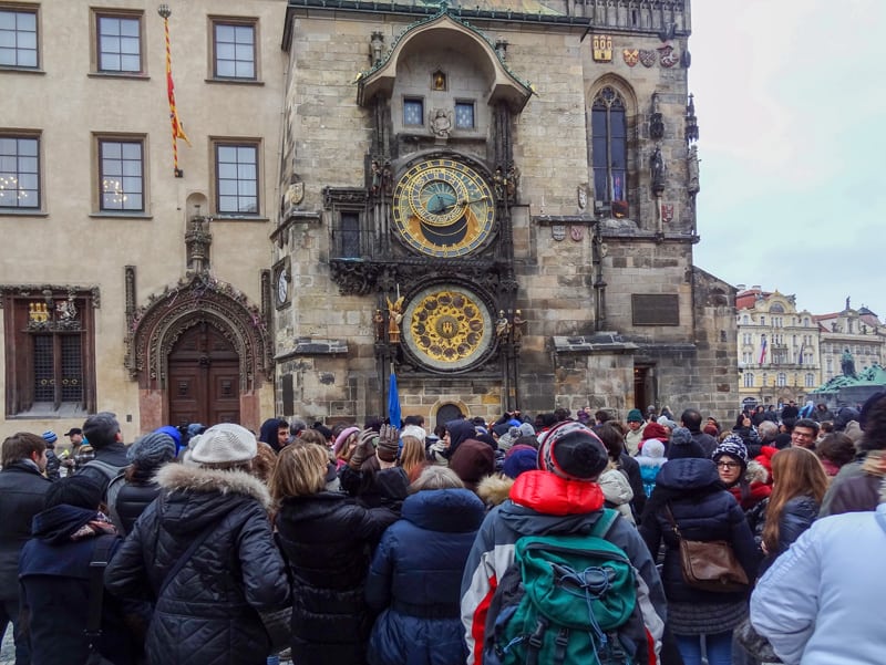 a crowd of people looking at a ancient clock on an old building in Prague in winter