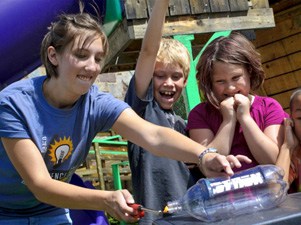 a young woman showing two children a science experiment 