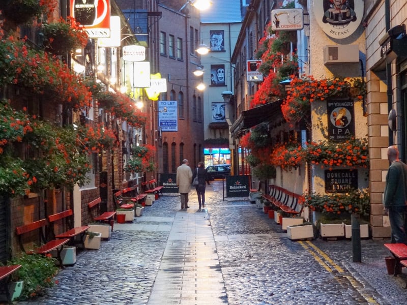 Two people walking down a quiet street in the evening in Belfast, where there are flowers on the walls.